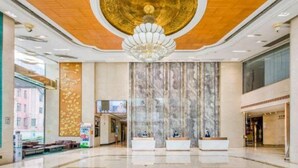 A spacious lobby with a marble reception desk, a large chandelier, and a television screen on the wall.