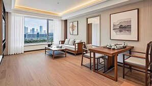 A modern hotel room with a city view, a sofa, a dining table, and artwork on the walls.