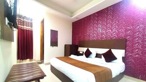 A hotel room with a bed, a small table, and a red patterned wall. - HOTEL AVSK (New Delhi)