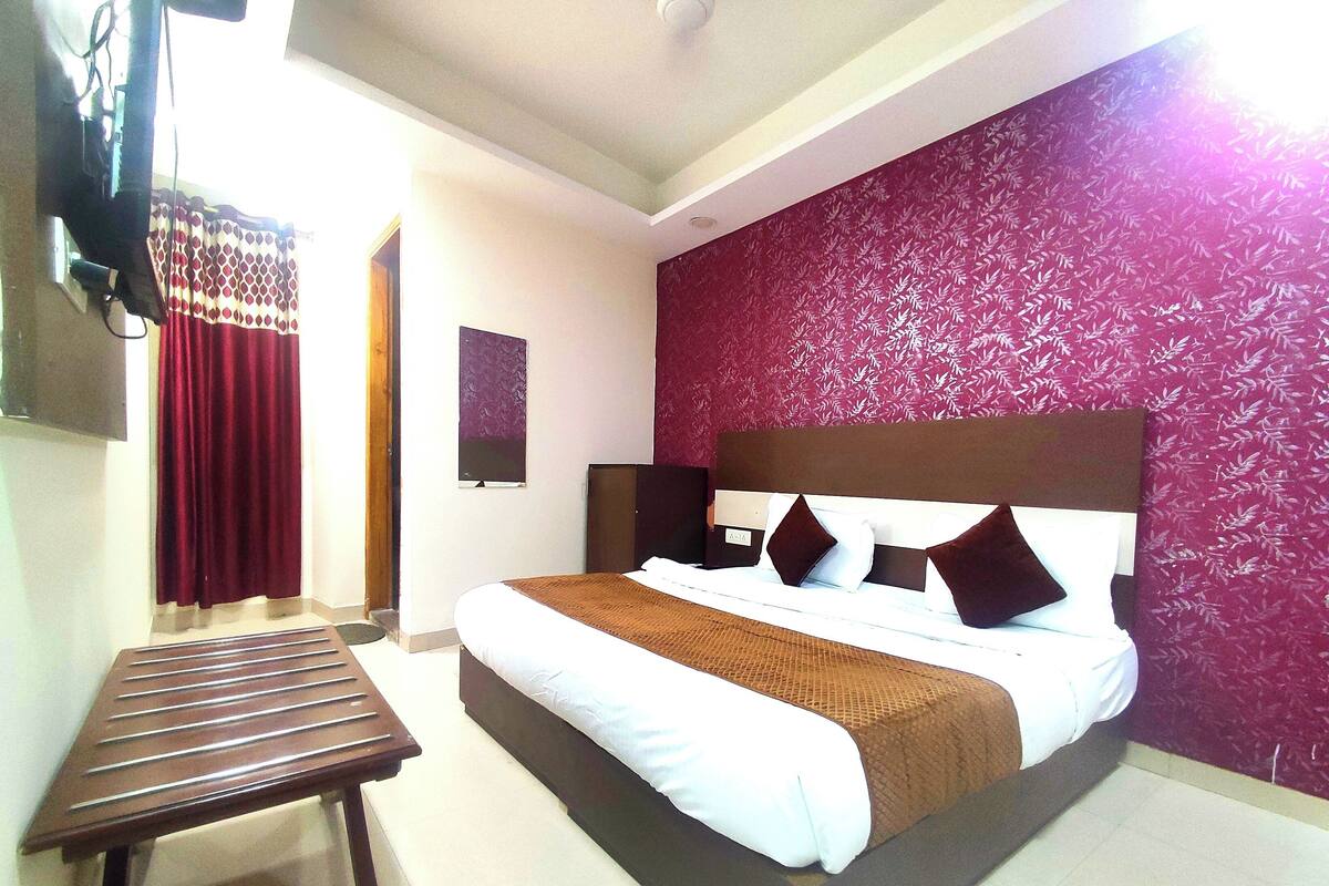A hotel room with a bed, a small table, and a red patterned wall.