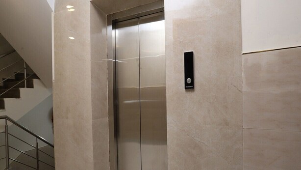 A modern elevator with a metallic finish, adjacent to a staircase with metal railings. - HOTEL AVSK (New Delhi)