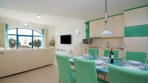 A modern living room with a sofa and a dining area with green chairs and a table set for two. - Ocean Dream Apartment (Piran)
