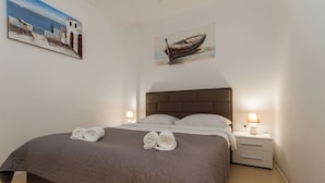 A neatly made bed with a brown quilt, two rolled towels, and a nightstand with a lamp. - Ocean Dream Apartment (Piran)