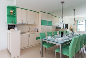 Eine moderne Küche mit Essbereich, grünen Stühlen und einem Glastisch, gedeckt für sechs Personen.