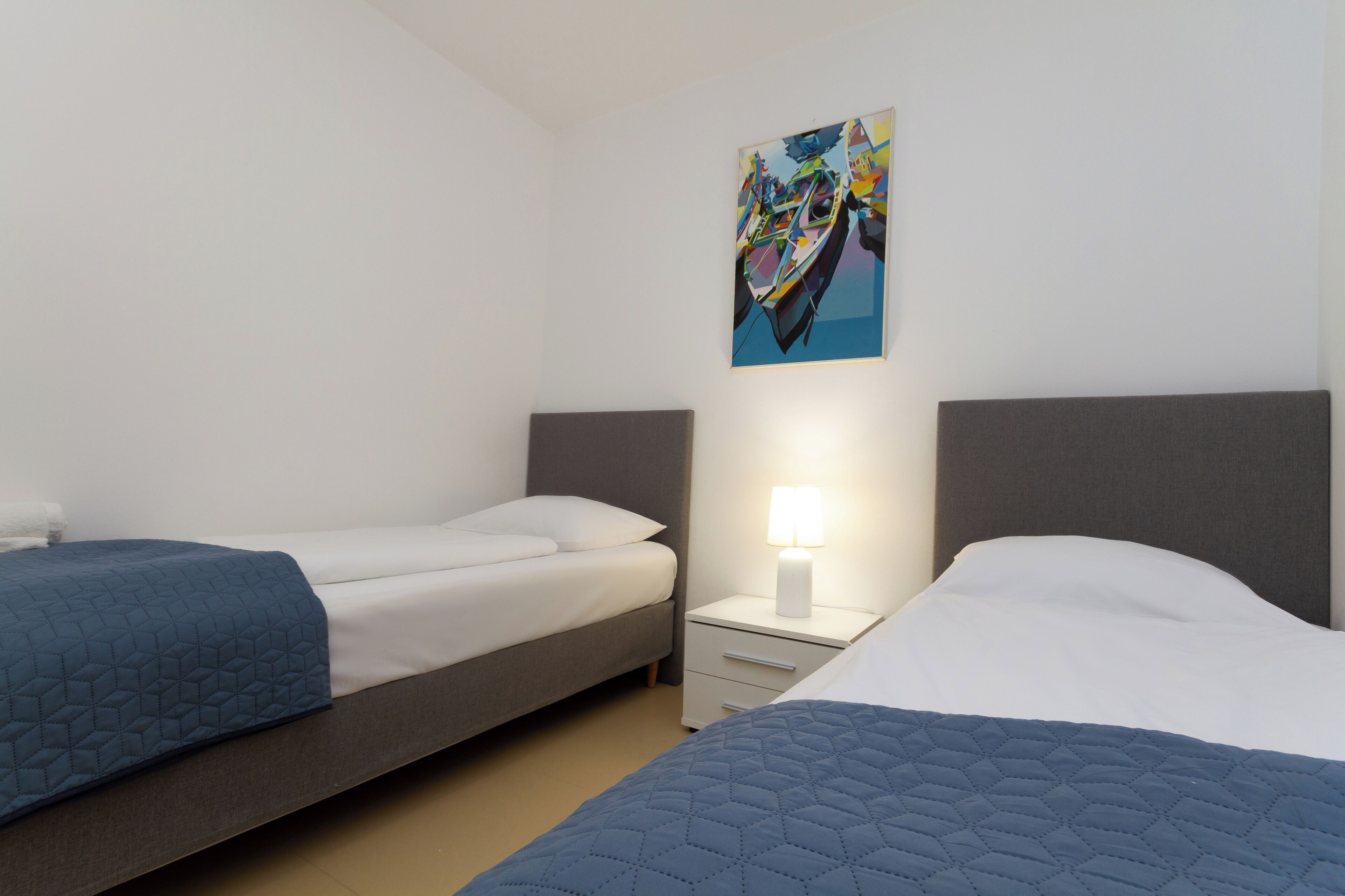 Une chambre d’hôtel avec deux lits simples, une table de chevet avec une lampe et une peinture abstraite aux couleurs vives accrochée au mur.