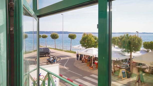A view from inside a building overlooking a waterfront area with outdoor seating and a parked scooter. - Ocean Dream Apartment (Piran)