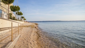 A pebbled beach with a concrete walkway and palm trees. - Ocean Dream Apartment (Piran)
