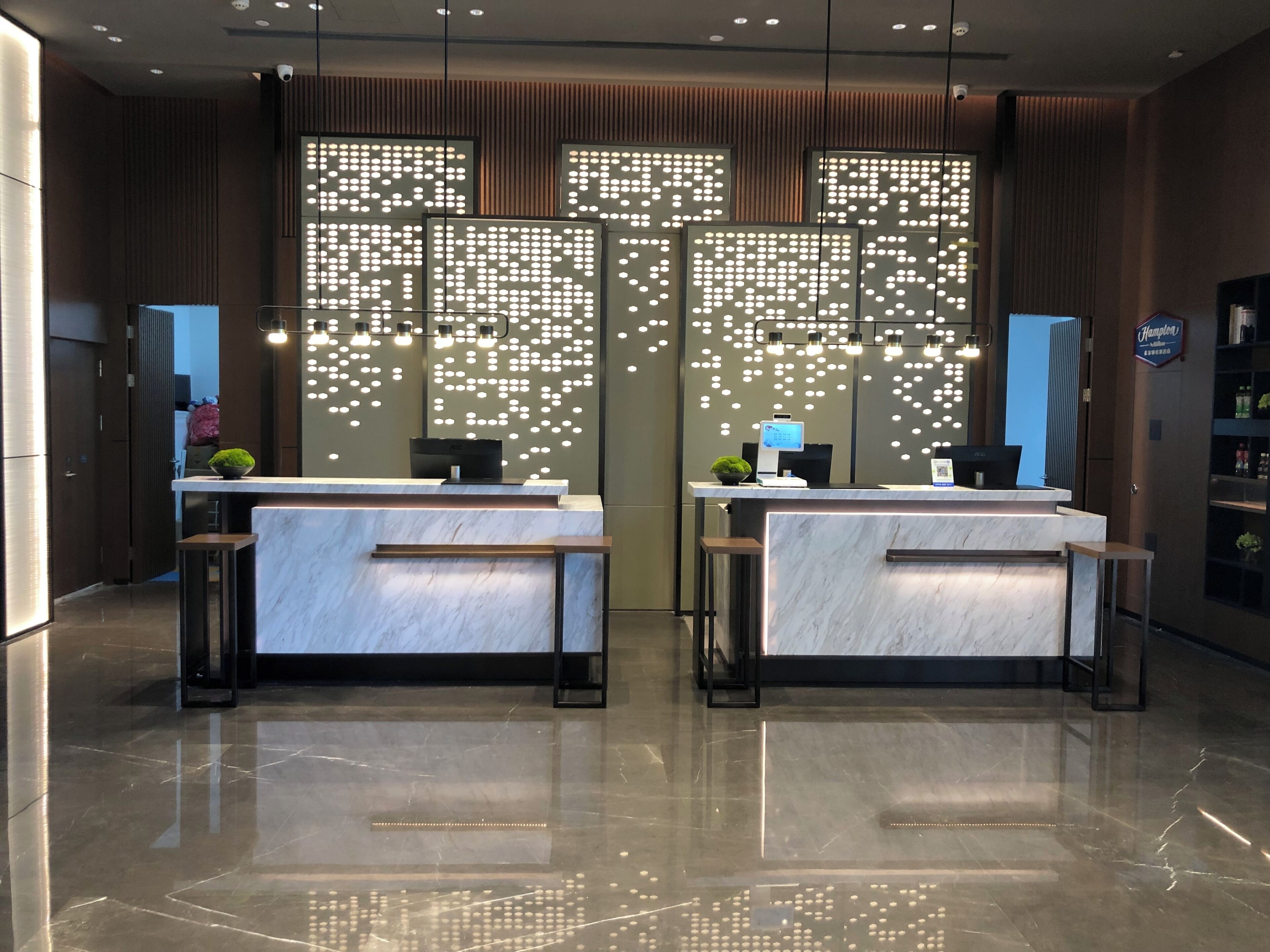 A modern hotel reception area with marble counters, a digital screen, and a decorative light panel.