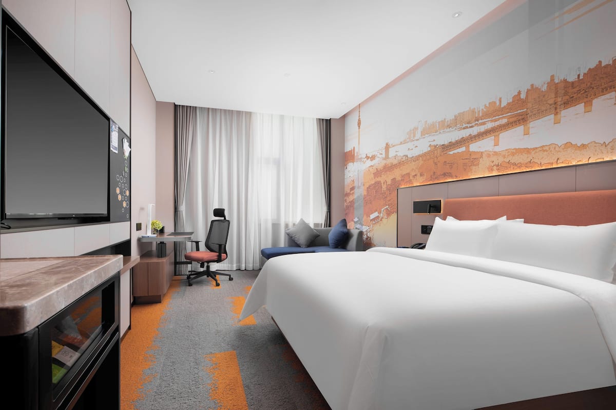 Habitación de hotel con una cama grande, un escritorio con una silla, un televisor y un mural con vista a la ciudad en la pared.