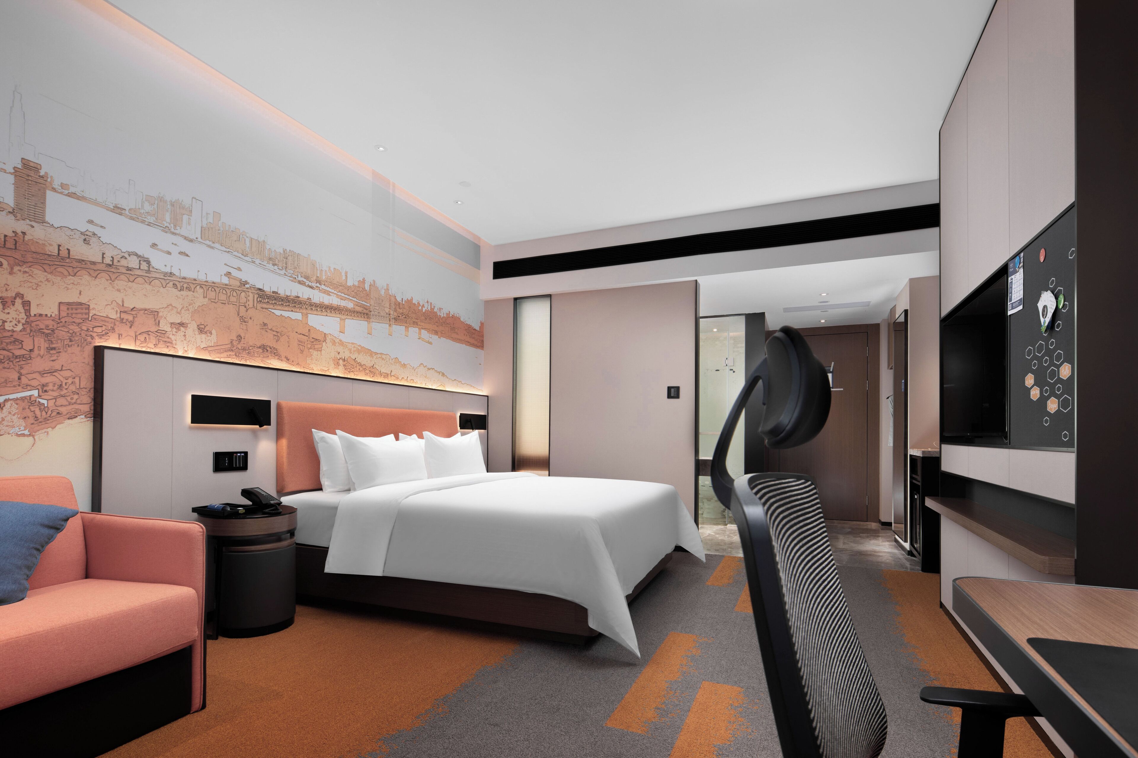 A modern hotel room with a large bed, a sofa, a desk, and a TV.