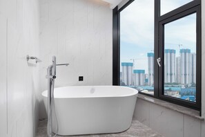 Un baño moderno con una bañera independiente, un cabezal de ducha y un ventanal con vistas a la ciudad.