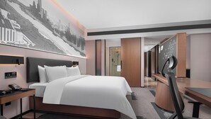 Une chambre d’hôtel moderne avec un grand lit, un bureau et une fresque représentant un paysage urbain sur le mur.