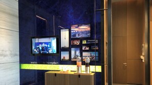 Un espace d’accueil moderne doté d’un écran numérique affichant une vue sur la ville, d’un comptoir d’accueil et d’une enseigne indiquant : « Bienvenue à l’hôtel Hampton. »