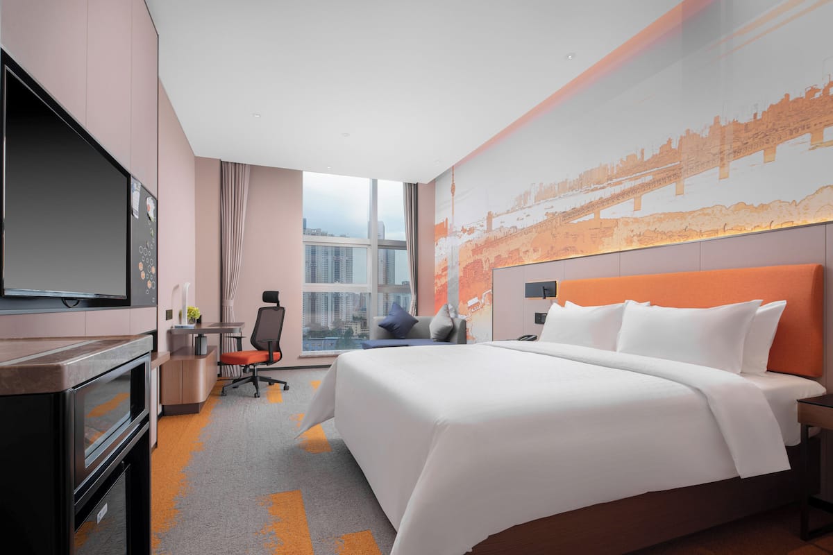 Habitación de hotel con una cama grande, televisión, escritorio y ventana con vistas a la ciudad.