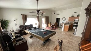 Un vaste salon comprenant une table de billard, un chien et un coin repas.