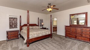 Une chambre à coucher avec un lit à baldaquin doté d’un ventilateur de plafond, une commode et un miroir.
