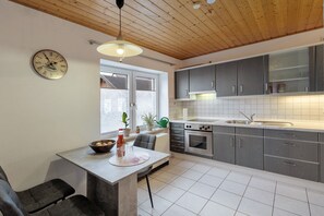 A modern kitchen with a wooden ceiling, a clock, and a dining area with a table and chairs.