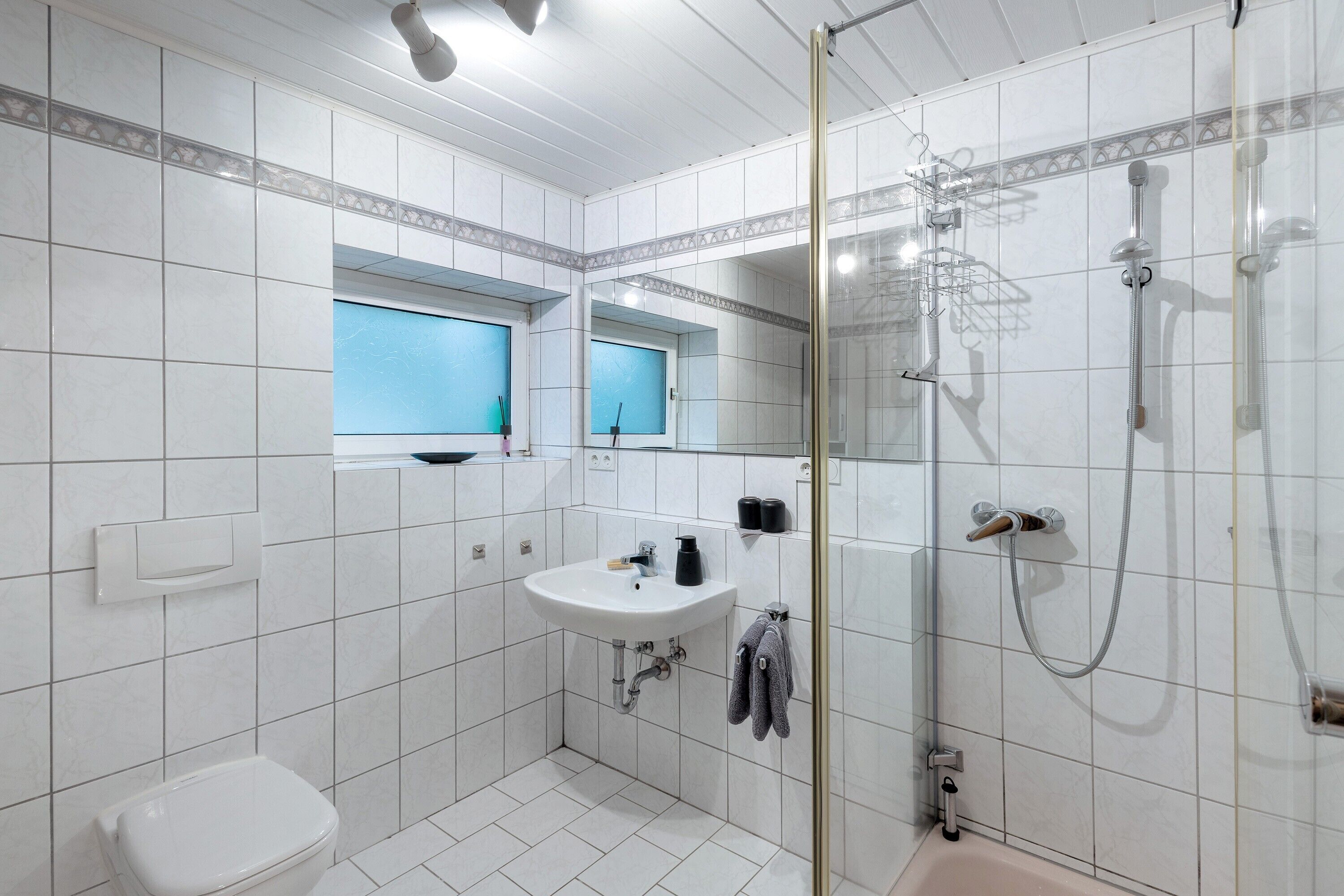 A bathroom with a toilet, sink, shower, and a window.