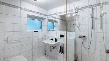 A bathroom with a toilet, sink, shower, and a window.