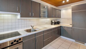 Une cuisine avec des meubles gris, un évier en acier inoxydable, un four encastré et un plafond en bois.