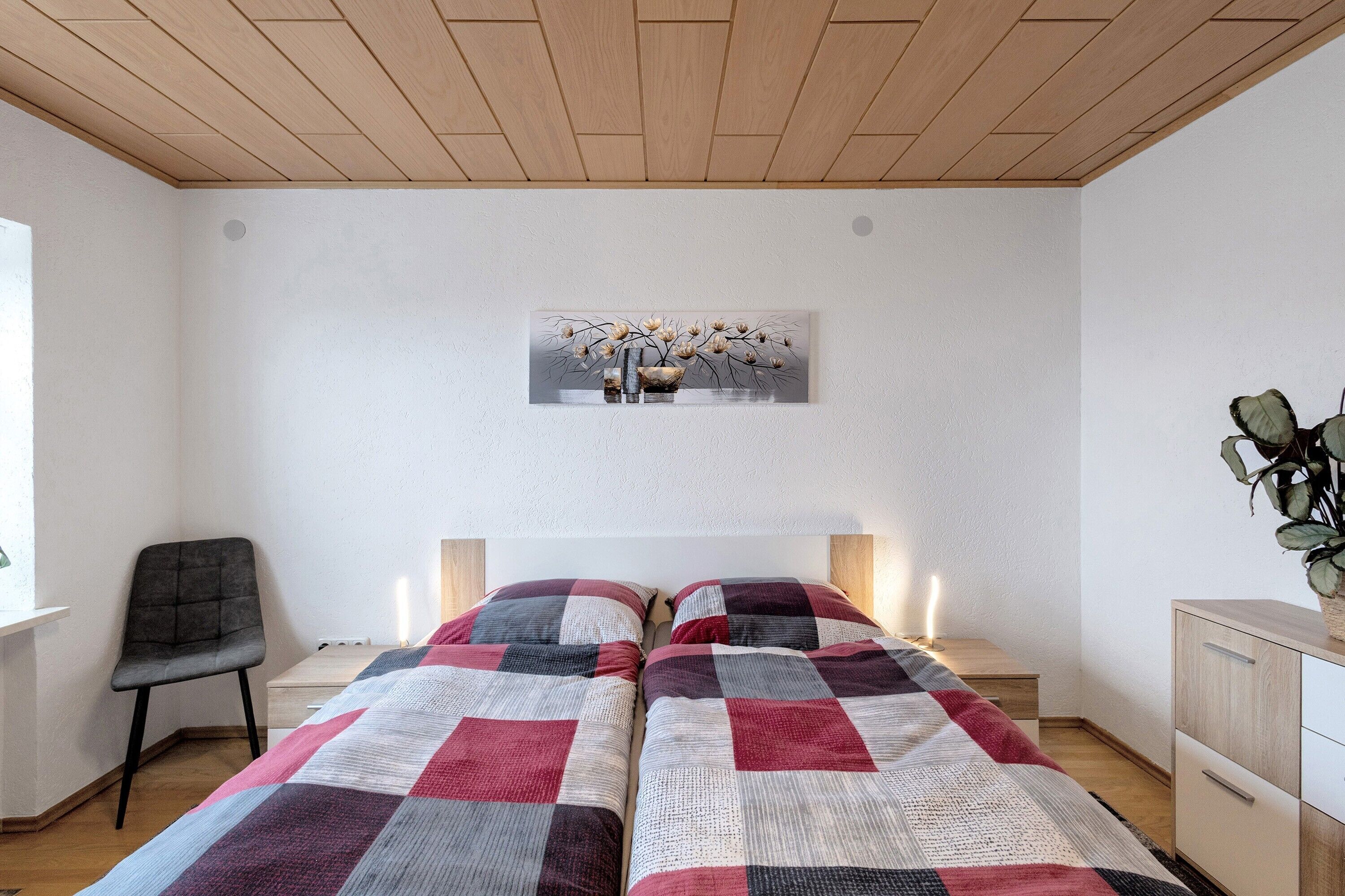 Una camera da letto con due letti, una sedia, una scrivania, una pianta e un quadro appeso al muro.