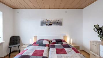 Una camera da letto con due letti, una sedia, una scrivania, una pianta e un quadro appeso al muro.
