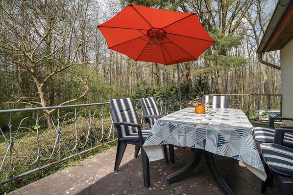 Eine Terrasse im Freien mit Tisch, Stühlen und einem roten Sonnenschirm.