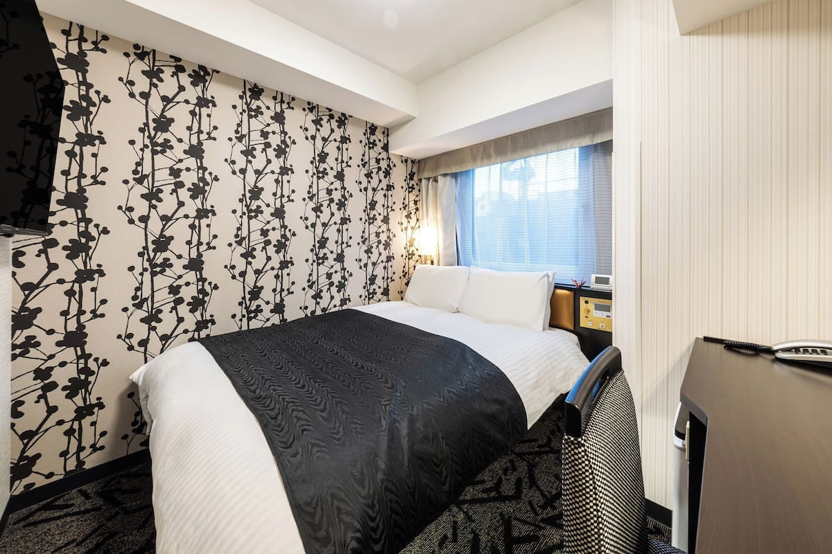 A hotel room with a large bed, a desk with a computer, and a window with curtains.