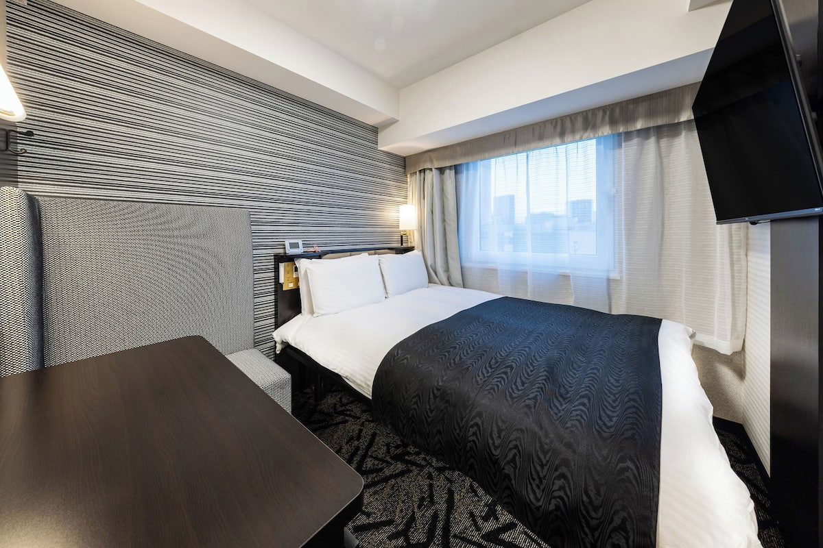 A hotel room with a bed, a desk, a TV, and a window with curtains.
