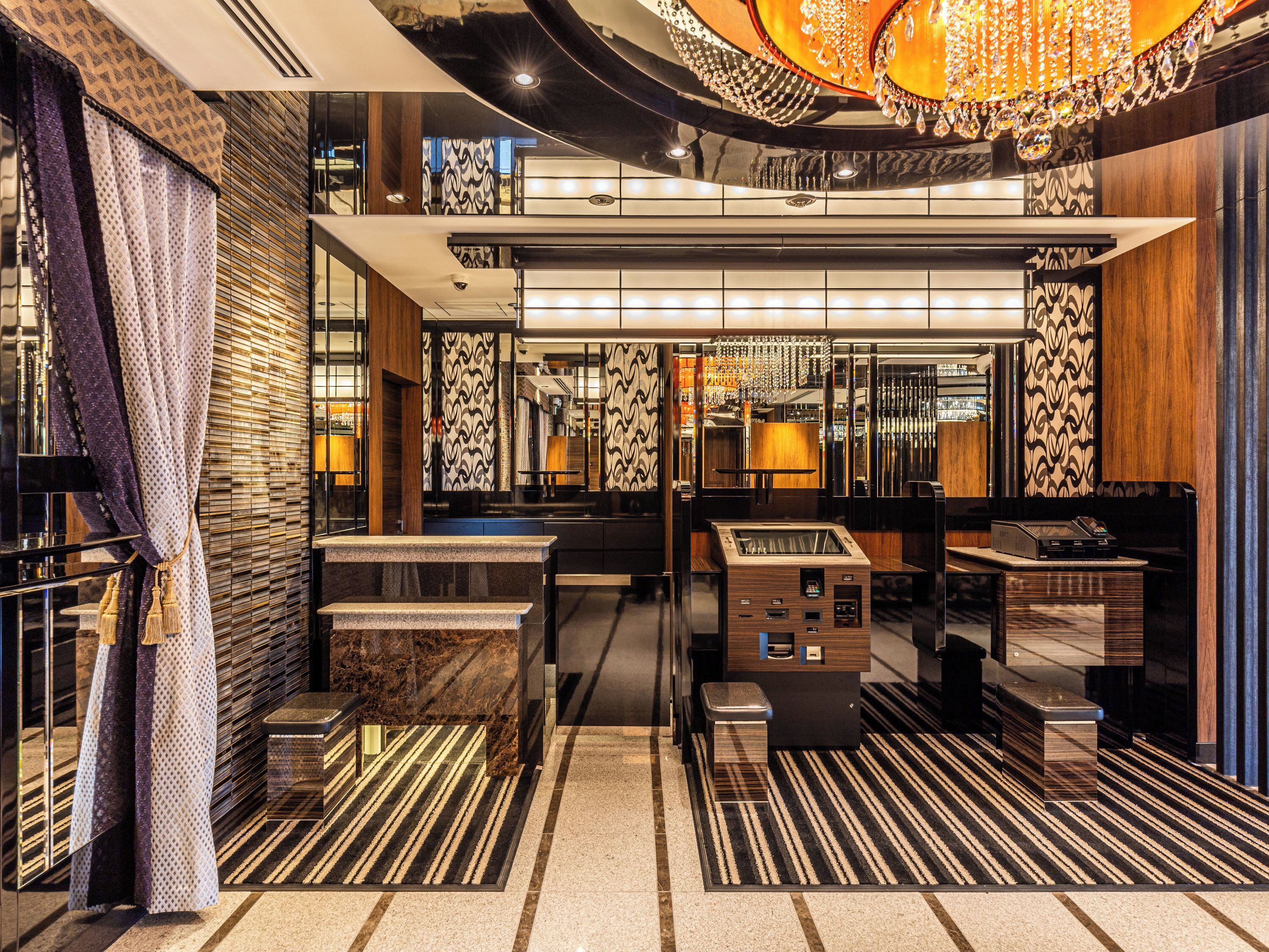 A luxurious lobby with a marble reception desk, a modern chandelier, and patterned wall designs.