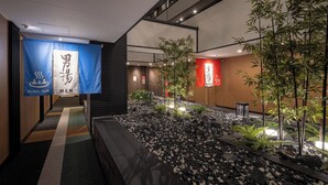 A public bath area with signage for men and women, a tiled floor, and a rock-lined pathway. - APA Hotel Akabane Iwabuchi Ekimae (Tokyo)