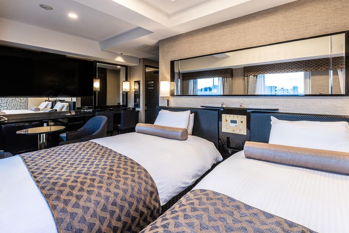 A hotel room with two beds, a desk, a TV, and a city view.