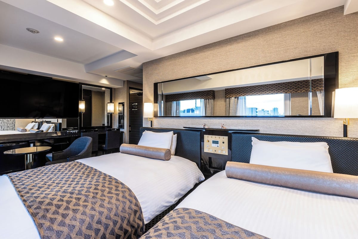 A hotel room with two beds, a desk, a chair, a TV, and a large window.