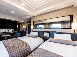 Habitación de hotel con dos camas, un escritorio, una silla, un televisor y un ventanal amplio.