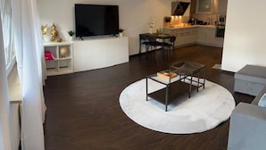 Una sala moderna con una televisión de pantalla plana, una mesa de centro redonda y un comedor.