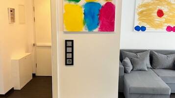 Ein modernes Wohnzimmer mit einem grauen Sofa, einem farbenfrohen abstrakten Gemälde und einer Tür mit Lichtschalter.