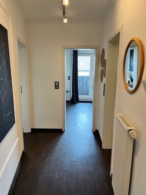 Ein Flur mit Heizkörper, Spiegel und einer Tür zu einem Zimmer mit Fenster und Vorhängen.