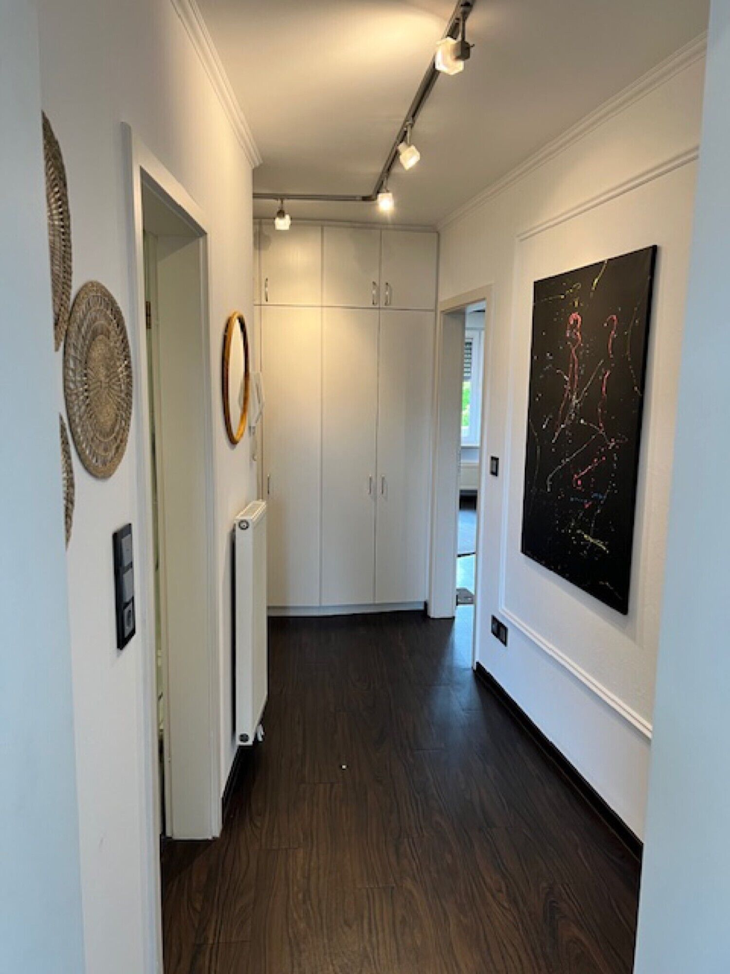 A hallway with a dark wooden floor, white walls, and a large abstract painting.