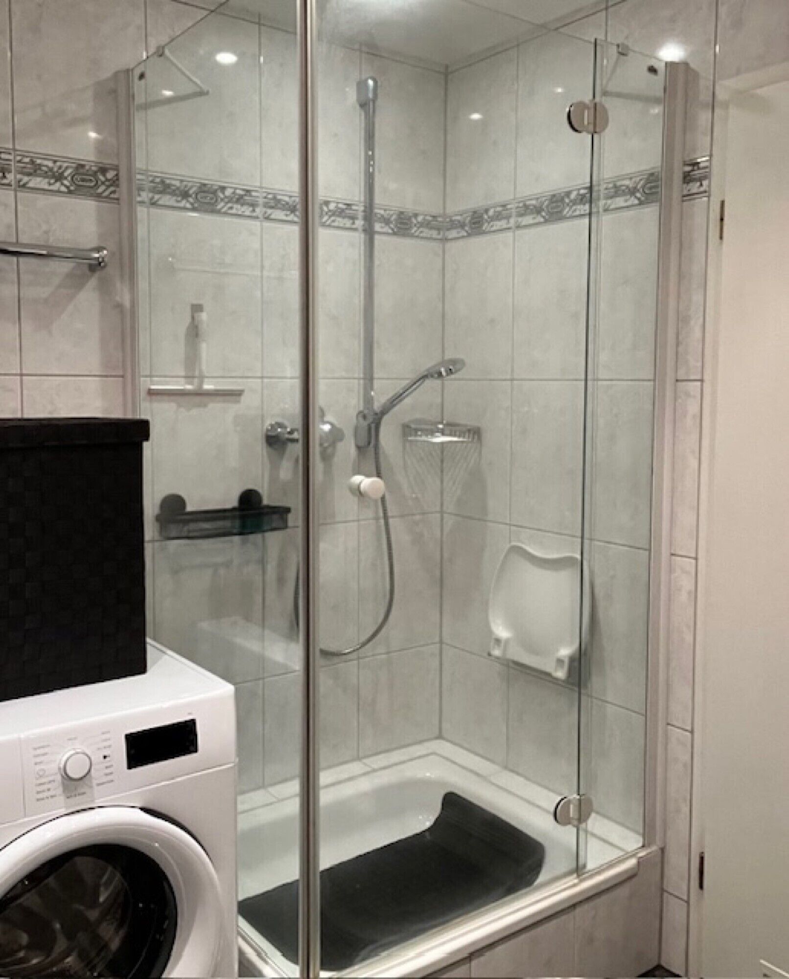Glastrukket brusekabine med et hvidt toilet og en vaskemaskine i det tilstødende område.