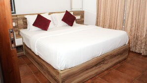 A neatly made bed with white linens and two red pillows, a wooden headboard, and a window with curtains. - Lakkidi Mist Resort (Vythiri)