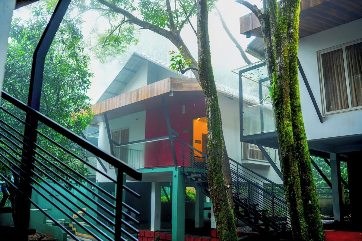 A modern building with a staircase, a tree with moss, and a view of a red building in the background.