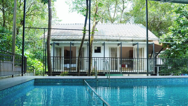 A swimming pool with a tiled edge, surrounded by a fence and trees. - Lakkidi Mist Resort (Vythiri)