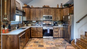 A kitchen with wooden cabinets, a stainless steel refrigerator, and a stone tile floor. - Cabin Retreat in the White Mountains of Arizona (Show Low)