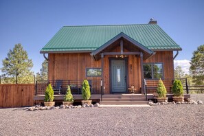 A wooden cabin with a green roof, a front door, and a small porch with potted plants. - Cabin Retreat in the White Mountains of Arizona (Show Low)