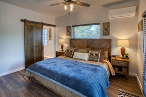 A bedroom with a bed, wooden headboard, two bedside tables with lamps, a ceiling fan, and a window with blinds.