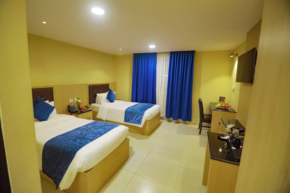 Habitación de hotel con dos camas, un escritorio, una silla y un televisor en la pared.