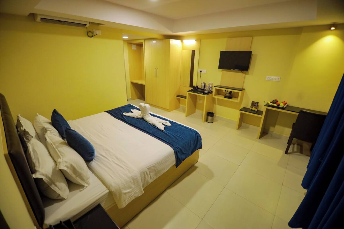 Habitación de hotel con cama, escritorio, silla, televisión y una mesita con una bandeja de fruta.