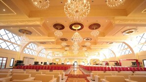 A grand hall with rows of red chairs, a central aisle, and ornate chandeliers. - MJ Avyanna Resort & Convention Centre (Anekal)