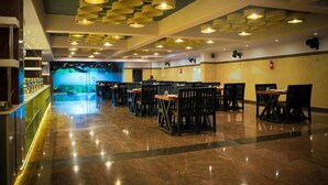 A spacious restaurant with a polished marble floor, multiple tables and chairs, and a ceiling with circular light fixtures. - MJ Avyanna Resort & Convention Centre (Anekal)