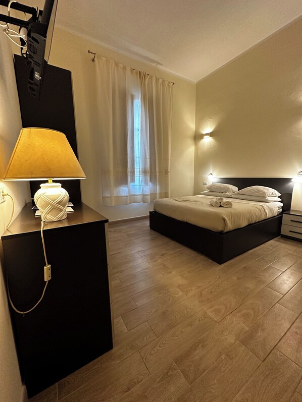 A hotel room with a bed, bedside tables, a desk with a lamp, and a window with curtains. - Double room with private bathroom in Terralba  (Oristano) - Helichrysum (Terralba)